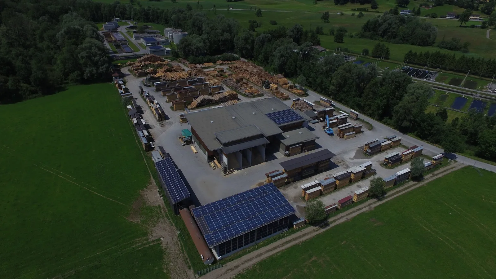 Schräges Luftbild des heutigen Werks: Weiterverarbeitungshalle, Trockenkammern und die Schnittholzstapel ringsum