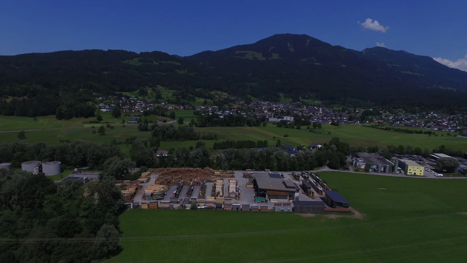 Luftbild über den Walgau: im Vordergrund das Sägewerk mit seinen Holzstapeln, dahinter die Ortschaft Satteins und die bewaldeten Hänge